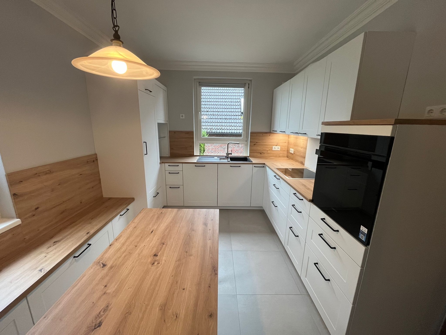 Einbauküche Häcker mit integrierter Sitzbank aus Küchenmöbeln, Holzoptik-Rückwand und Tisch in heller Wohnküche.