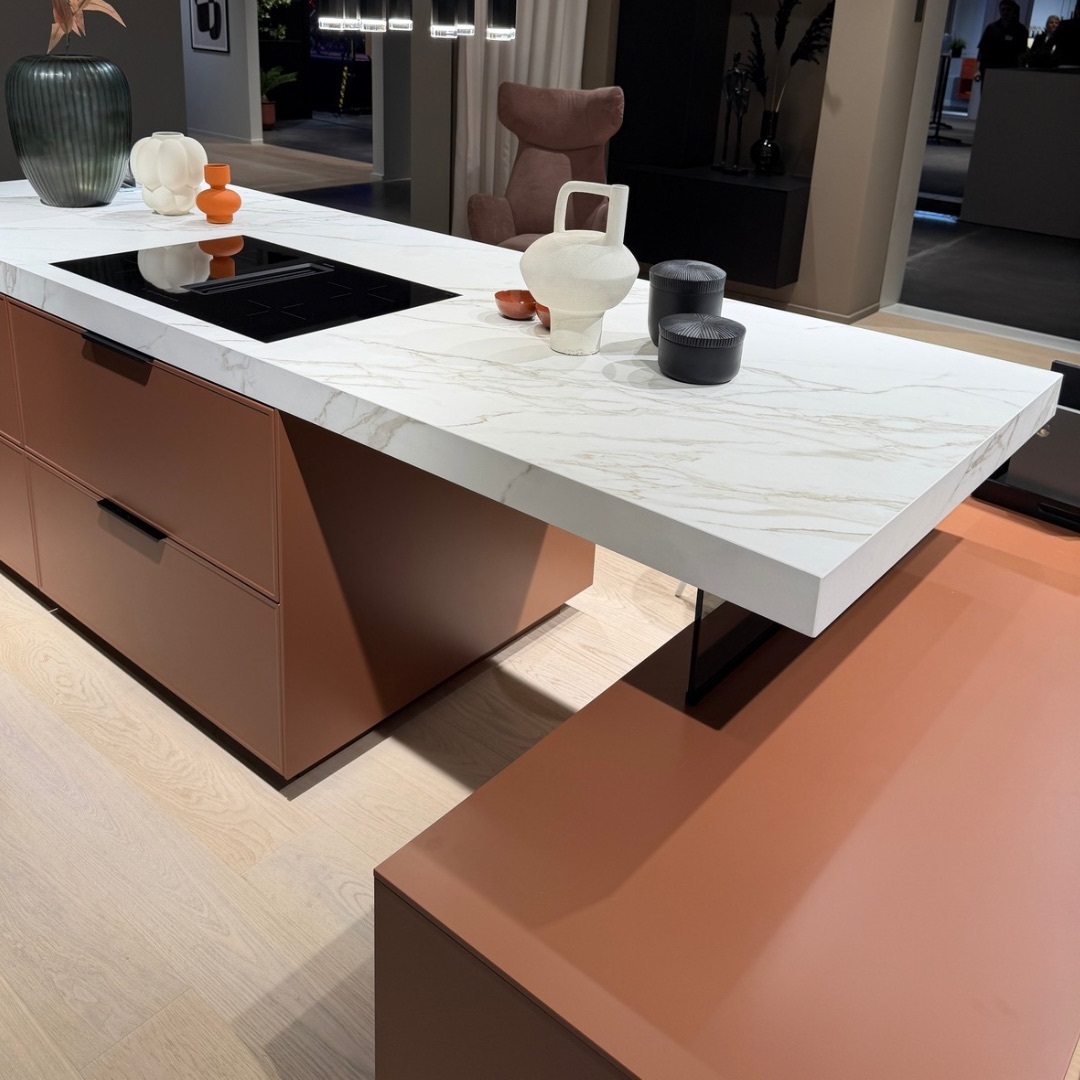 Moderne Kücheninsel mit weißer, marmorierter Keramik-Arbeitsplatte in matter Optik, kombiniert mit warmen Terrakotta-Unterschränken und minimalistischem Dekor.