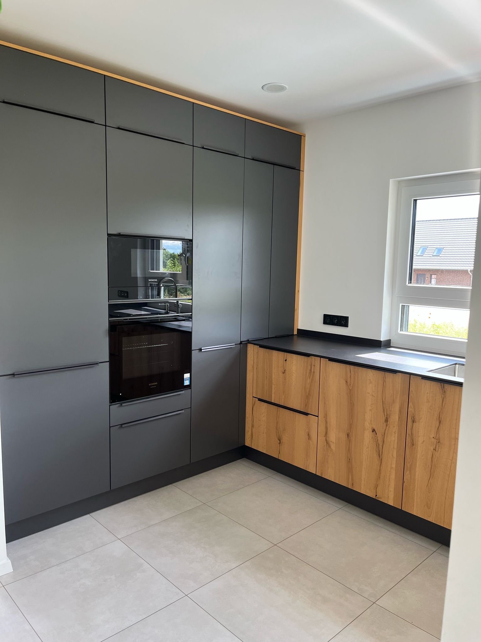 Häcker systemat Küche mit anthrazitfarbenen Fronten, Holzoptik-Unterschränken und schwarzer Arbeitsplatte – moderne Einbauküche in Hamburg.