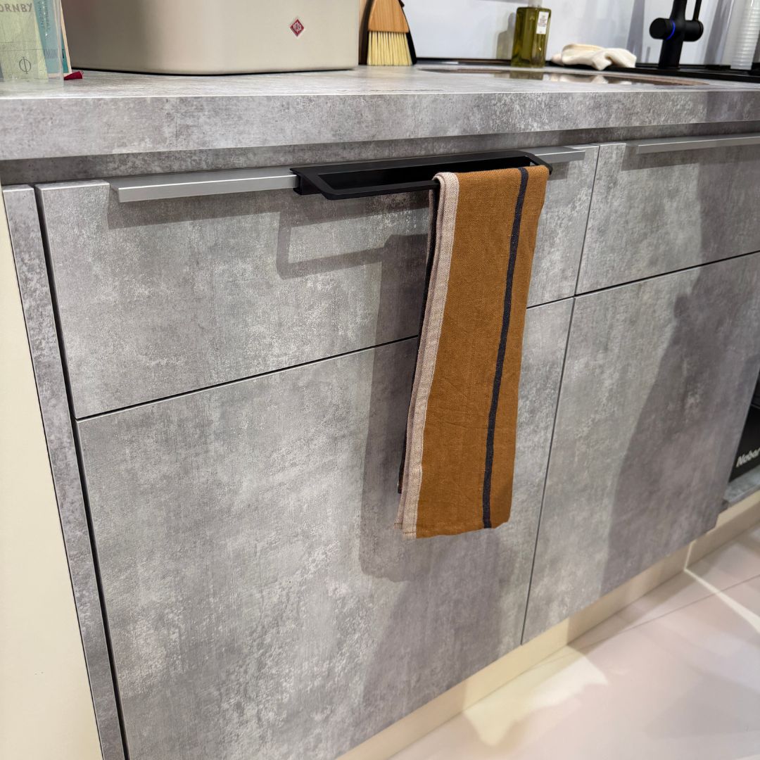 Moderner Handtuchhalter integriert in die Küchenfront mit grauer Betonoptik, funktionales Detail in der Küchenplanung, praktisch positioniert neben der Spüle für mehr Ordnung und Komfort.