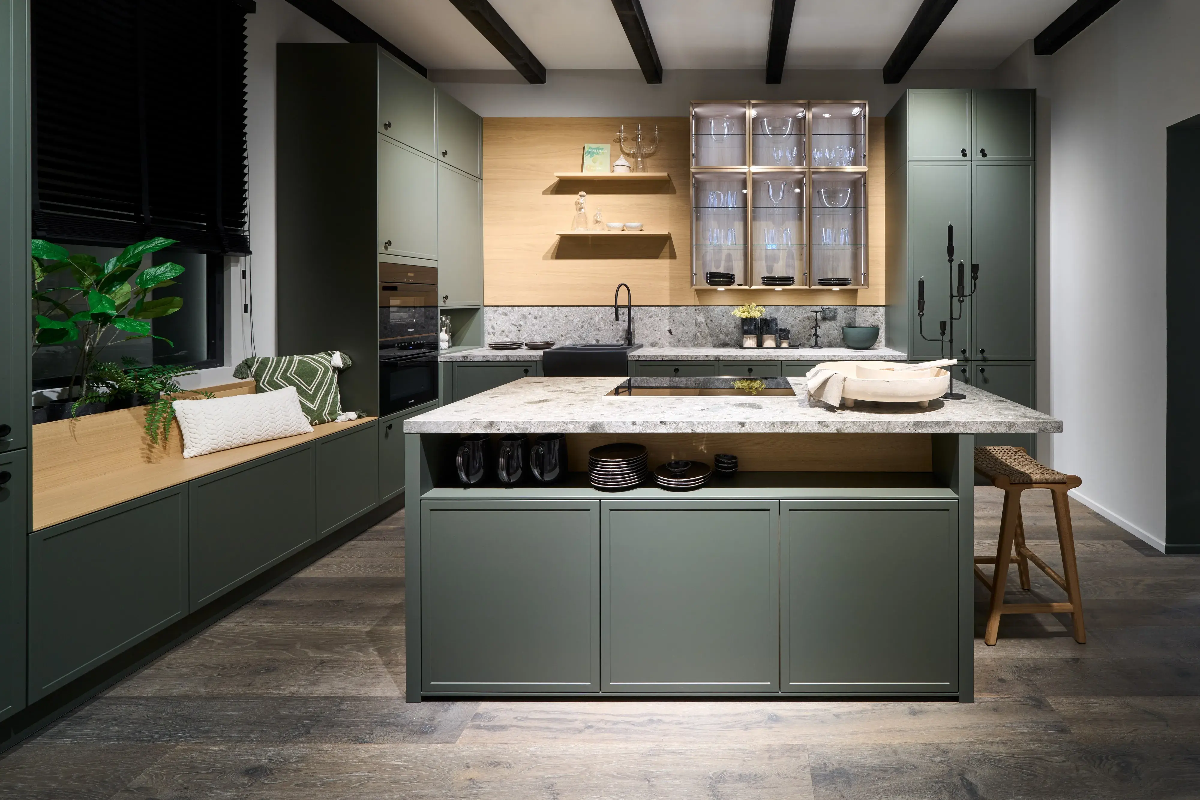 Häcker Systemat Küche mit grünen Fronten, heller Holzrückwand, Naturstein-Arbeitsplatte und integrierter Sitzbank