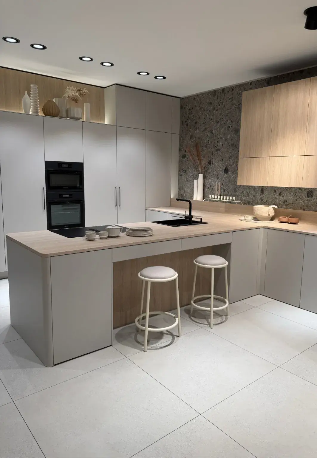 Moderne Küche in hellen Erdtönen mit grifflosen Fronten in Beige und Holzoptik, passender Arbeitsplatte und dunkler Steinrückwand.